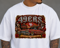 A white crewneck t-shirt featuring a large, detailed graphic print of the San Francisco 49ers. The graphic includes the team name in stylized lettering, a red and gold SF logo, a vintage car, and a skeleton character, all set against a gray background.